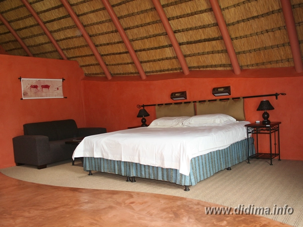 Comfortable double bed beneath the traditional thatched roof of a Didima Camp chalet
